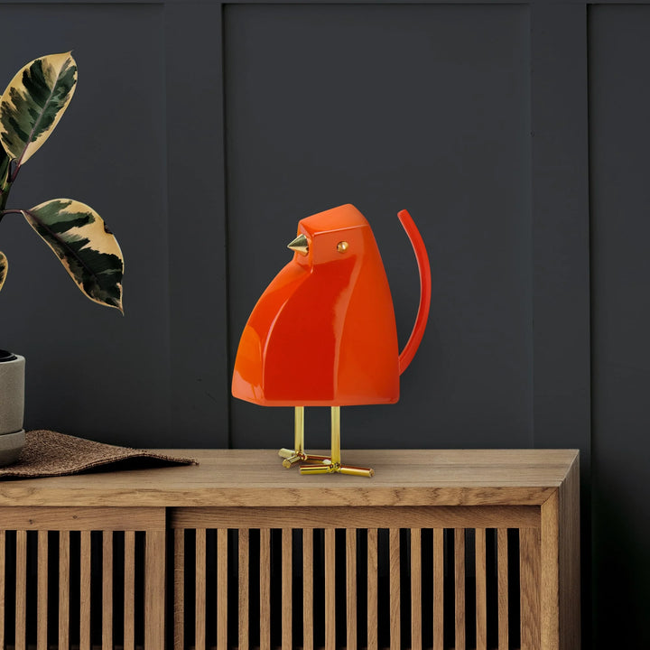 Red bird-shaped lamp on a wooden cabinet against a dark wall