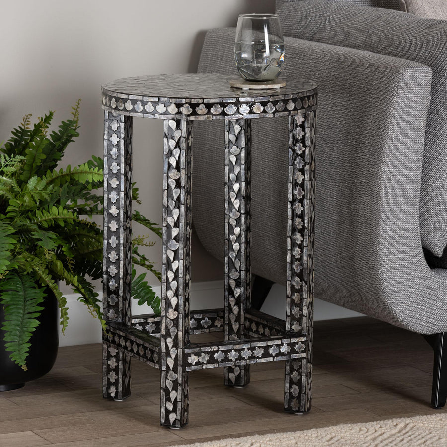 Decorative side table with intricate design next to a gray armchair and plant.