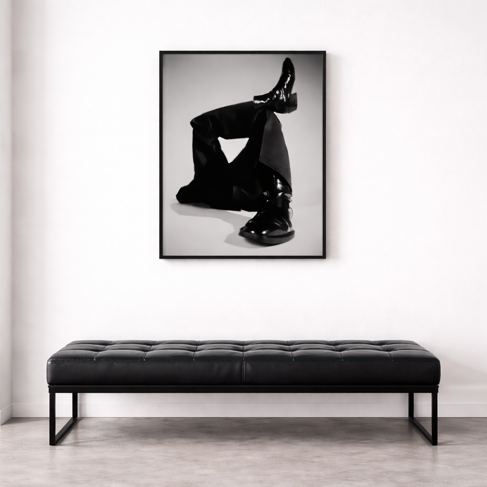 Black leather bench in front of a framed black and white art print on a white wall.