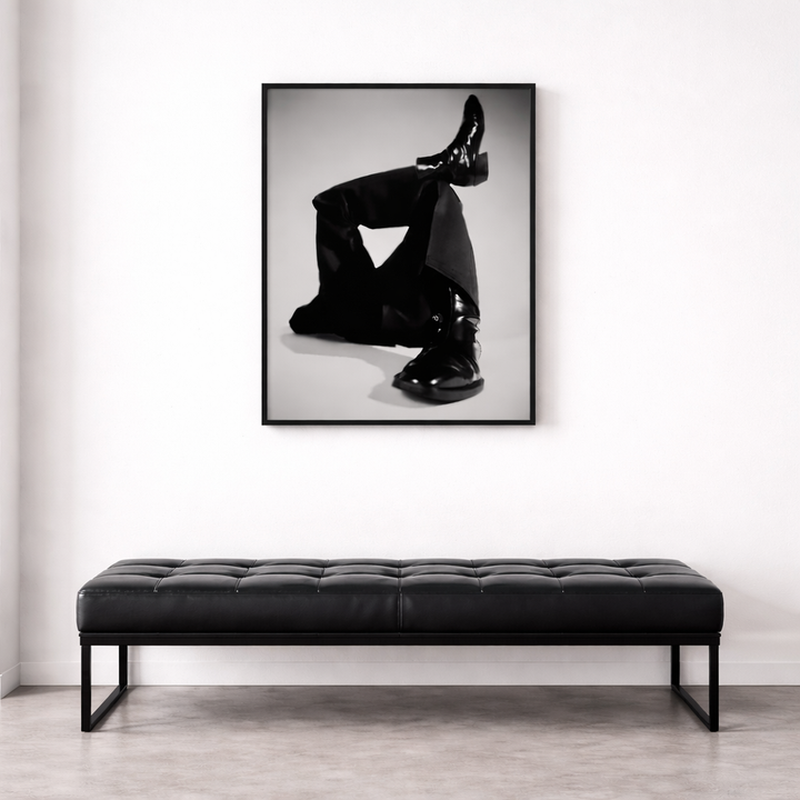 Black leather bench in front of a framed black and white art print on a white wall.