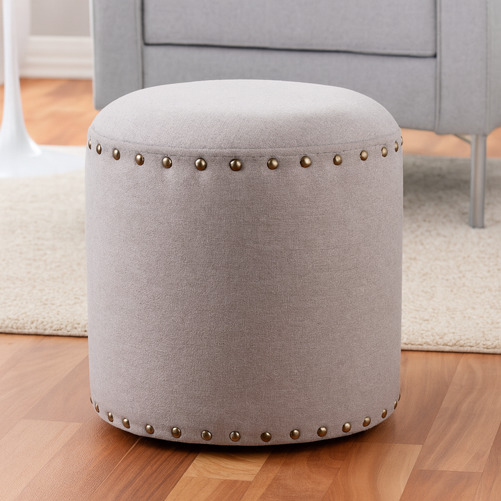 Gray upholstered ottoman with nailhead trim on a wooden floor.