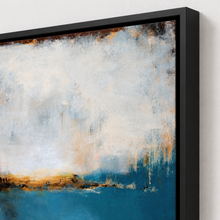 A framed abstract canvas print featuring textured brushstrokes of blue, cream, white, and warm brown tones, shown in a black frame against a light neutral wall.