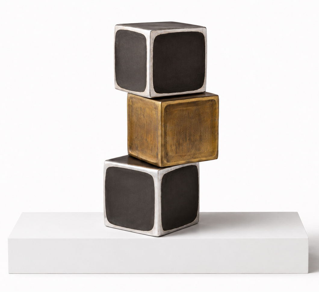 Three stacked decorative cubes on a white platform against a white background. The top and bottom cubes are dark charcoal gray with silver-toned edges, and the middle cube is metallic gold with a similar silver-toned edge. 