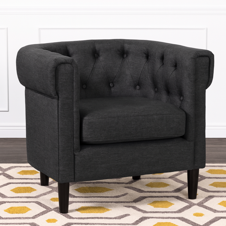 Dark gray tufted armchair on a patterned rug with a white wall background