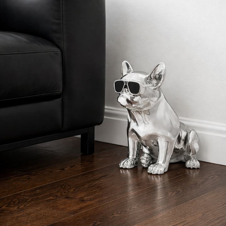 Silver dog figurine with sunglasses on a wooden floor next to a black leather couch.