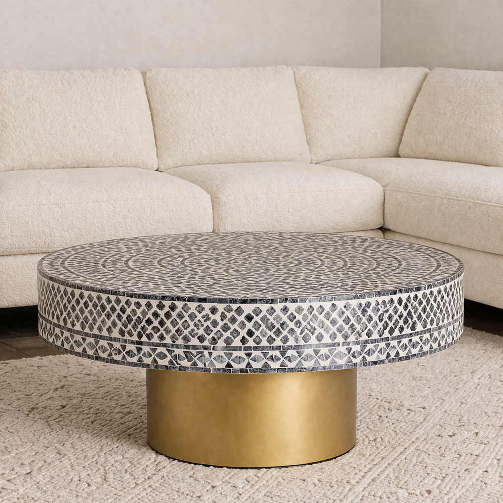 Round coffee table with mosaic top and gold base in front of a beige sectional sofa.