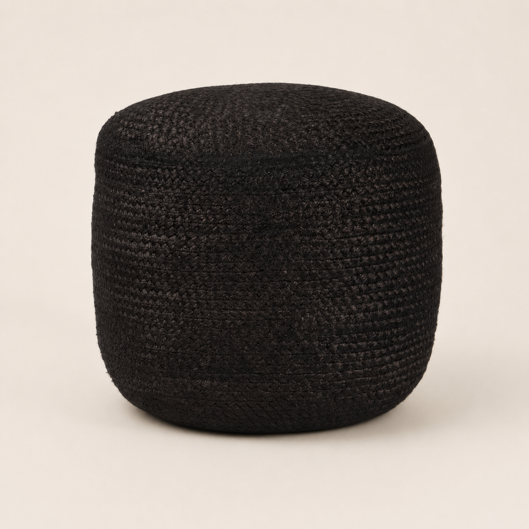 A round black woven pouf or ottoman with a textured, basket-like weave, photographed against a solid, warm off-white background.