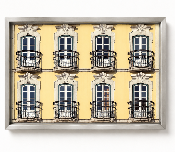 A framed photographic print of a yellow building facade with eight windows and black wrought-iron balconies, shown against a plain white background.