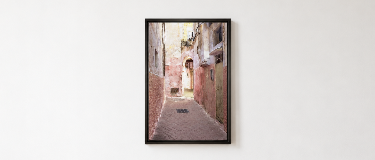 A framed vertical art print depicting a narrow European alleyway with warm-toned buildings, hung on a plain white wall.