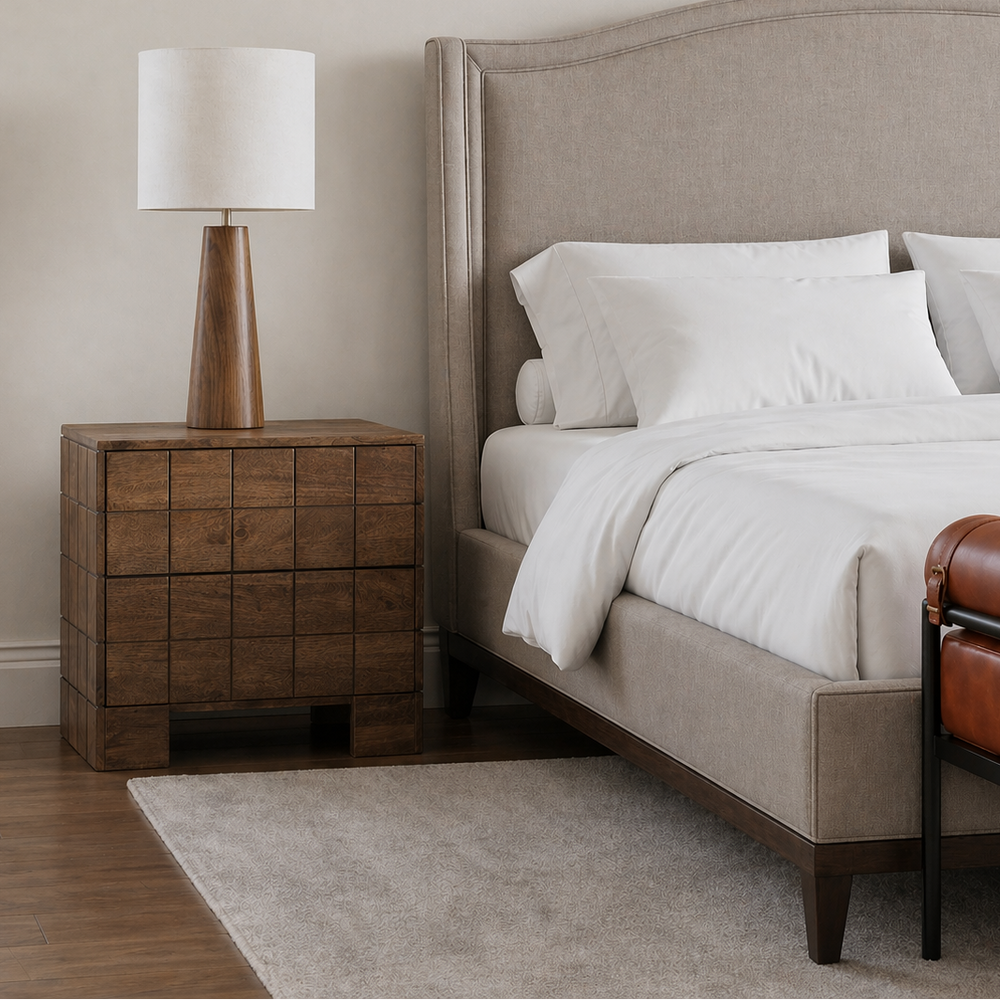 Neatly made bed with beige headboard and nightstand in a bedroom setting.