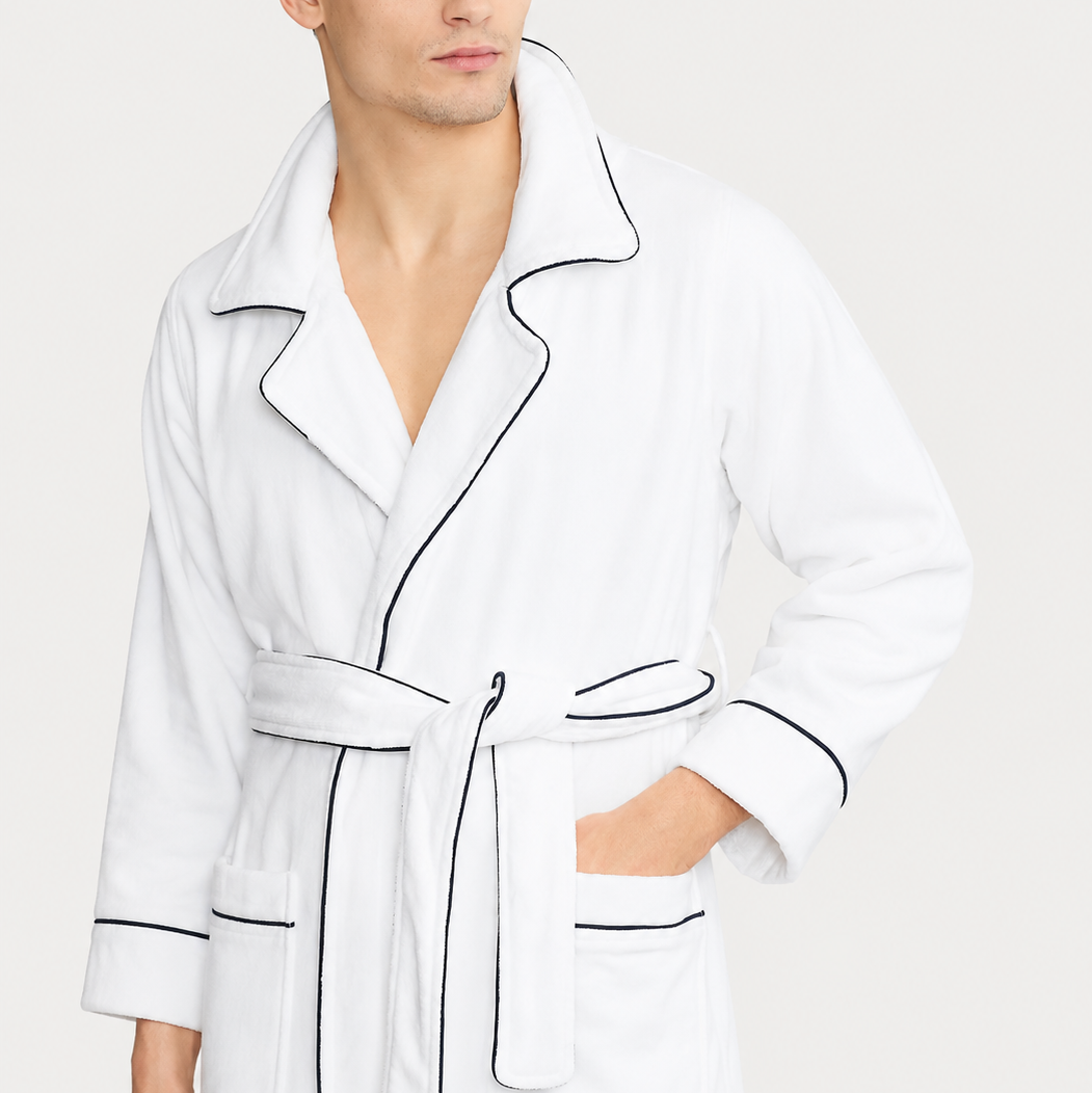 Man wearing a white robe with black piping on a light gray background