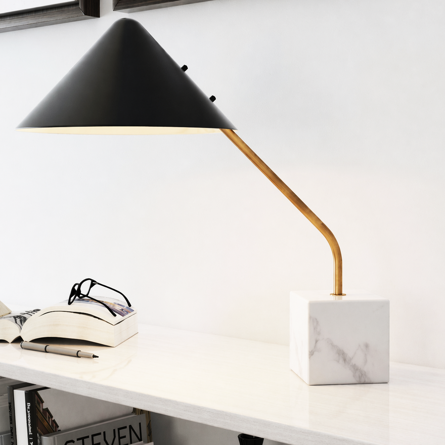 Modern desk lamp with black shade and gold arm on a white surface. 