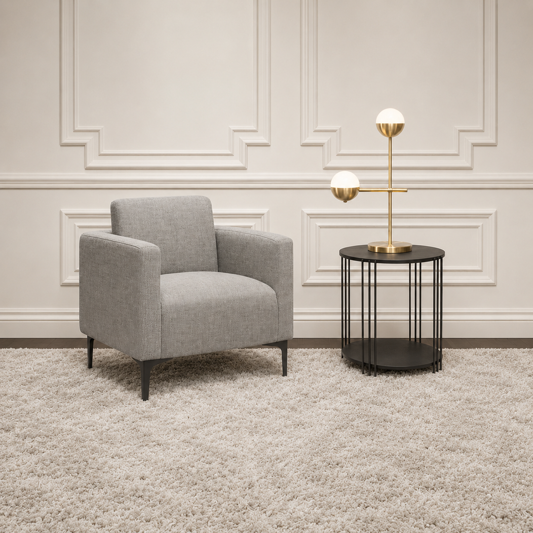 A modern gray upholstered armchair sits on a shag rug beside a black wire side table with a gold two-light floor lamp, set against a cream paneled wall.