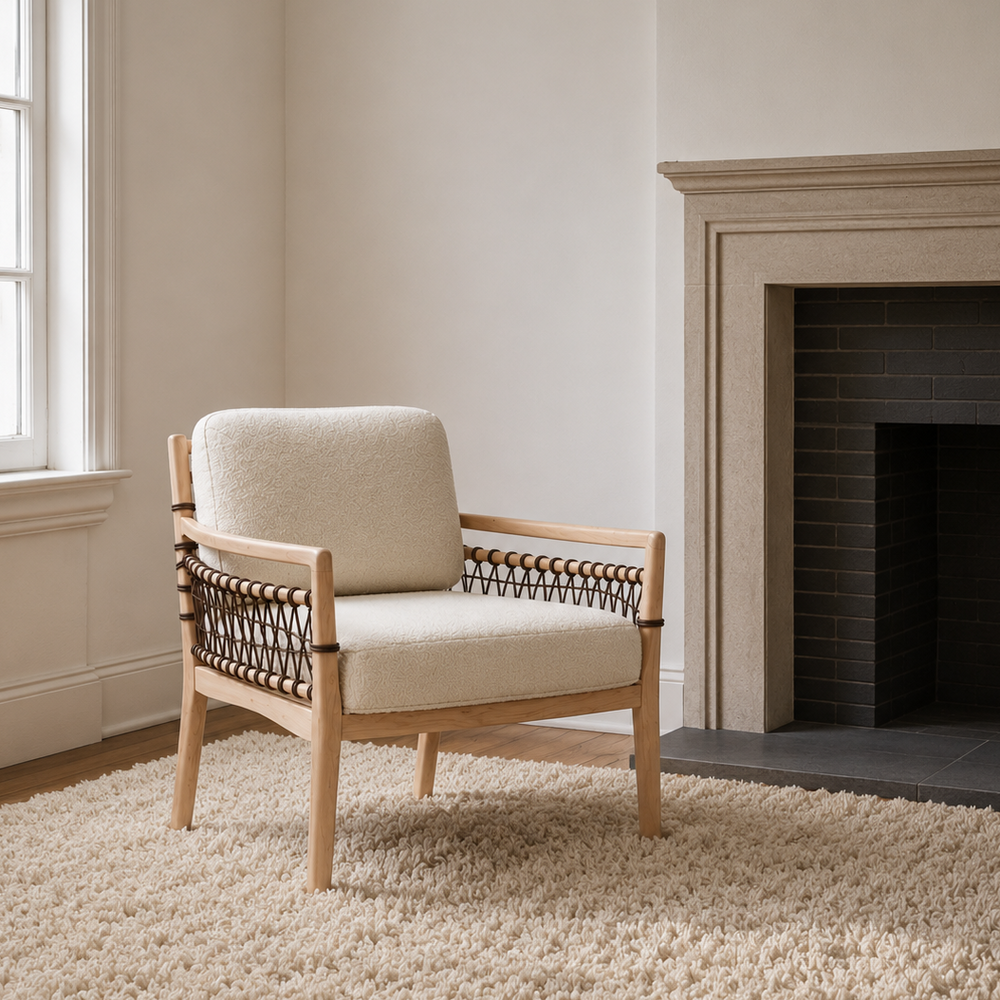 A mid-century modern accent chair with a cream bouclé seat and back cushion, light wood frame, and dark woven rope armrests, styled on a cream shag rug next to a fireplace.