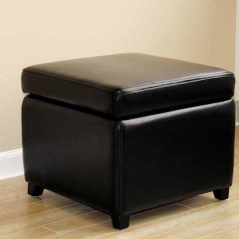 Black leather storage ottoman on a wooden floor with a beige wall background