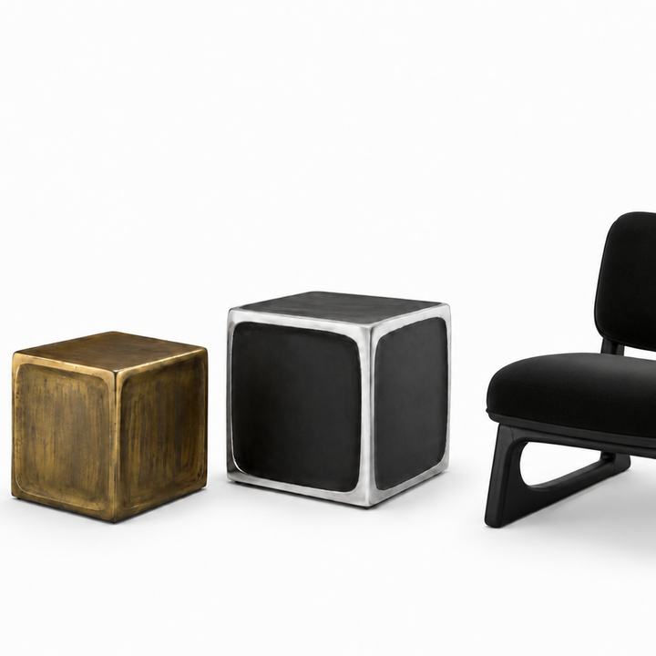 Three modern cube-shaped side tables or ottomans on a clean white background: one with a brushed brass/gold finish, one with a black and silver metallic frame, and one with a black upholstered cube chair. 