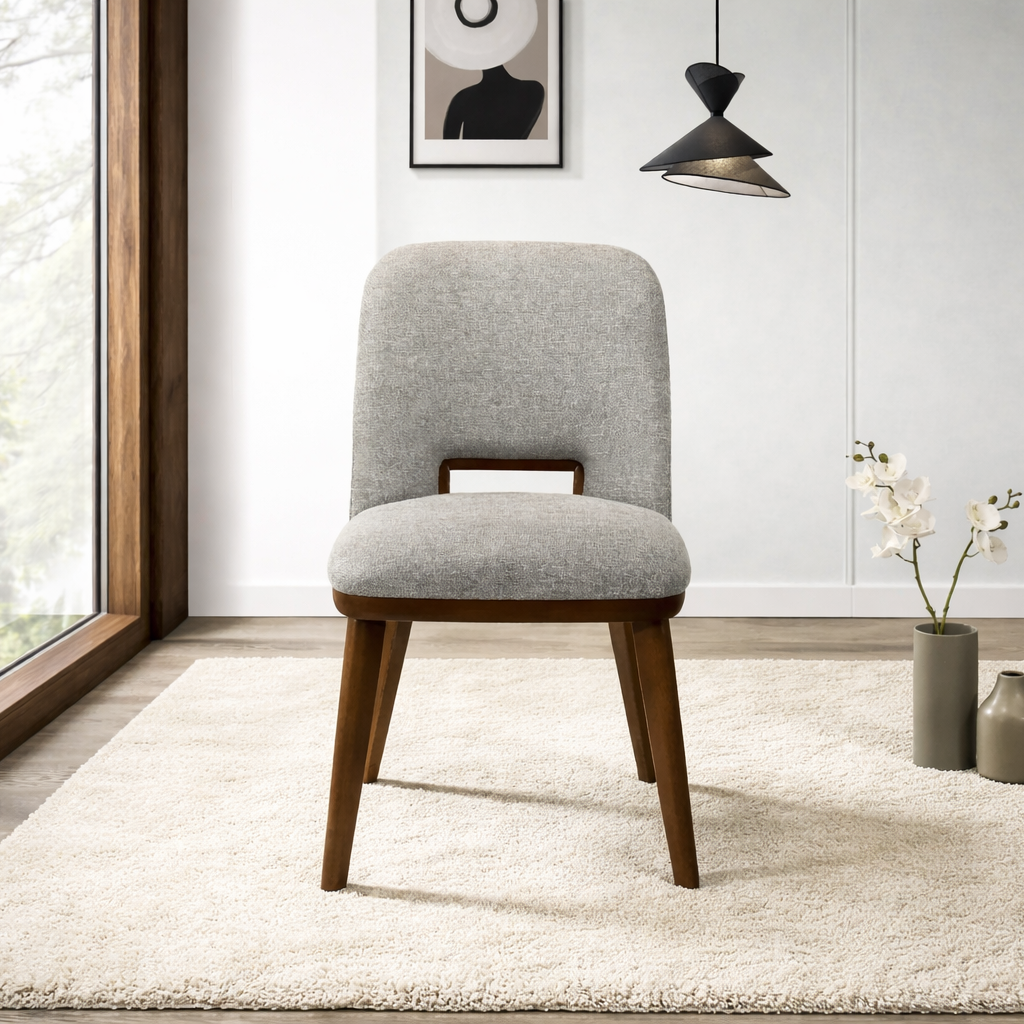 Gray upholstered chair with wooden legs in a modern room with large windows.