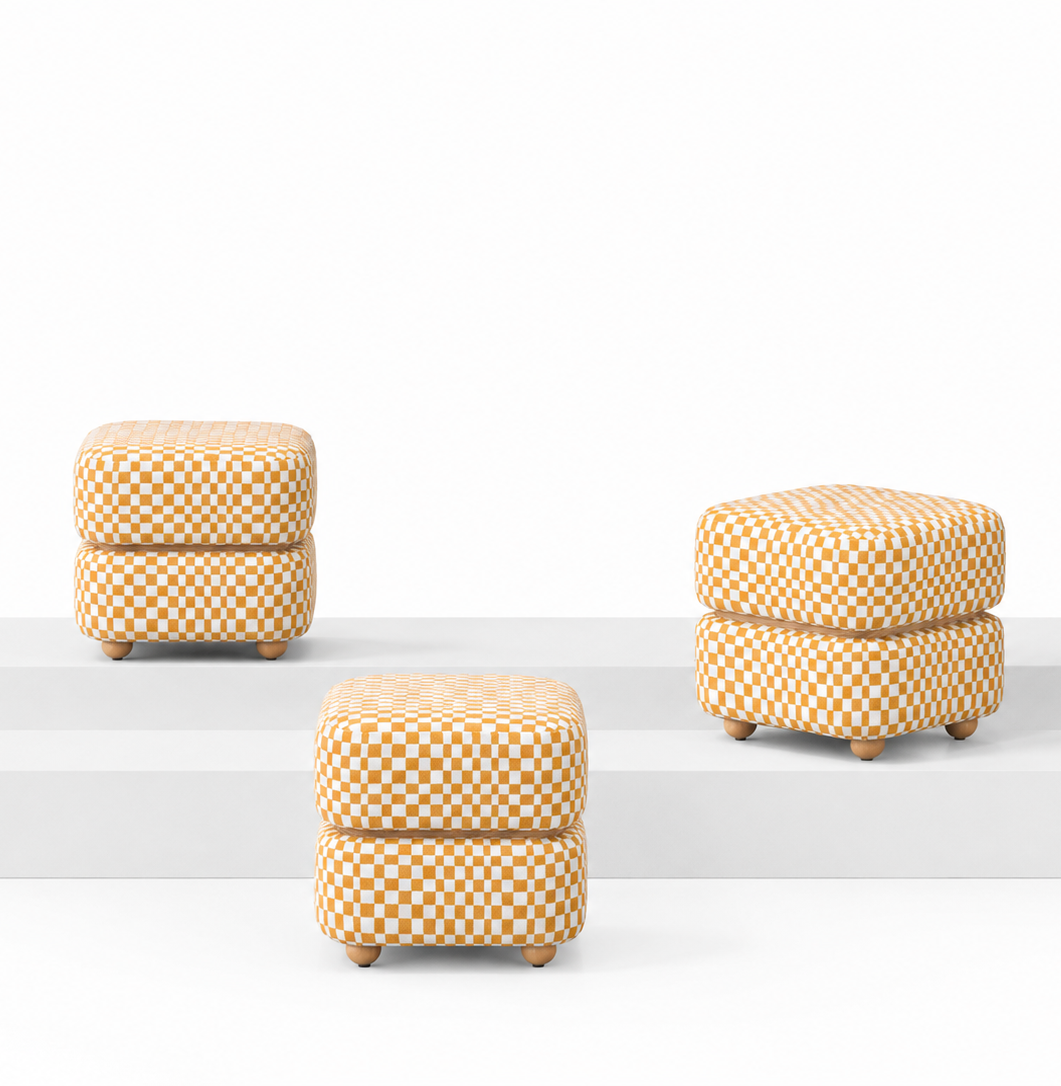 Three small square ottomans with a yellow and white checkerboard pattern and light wood legs, displayed on white tiered risers against a white background.  