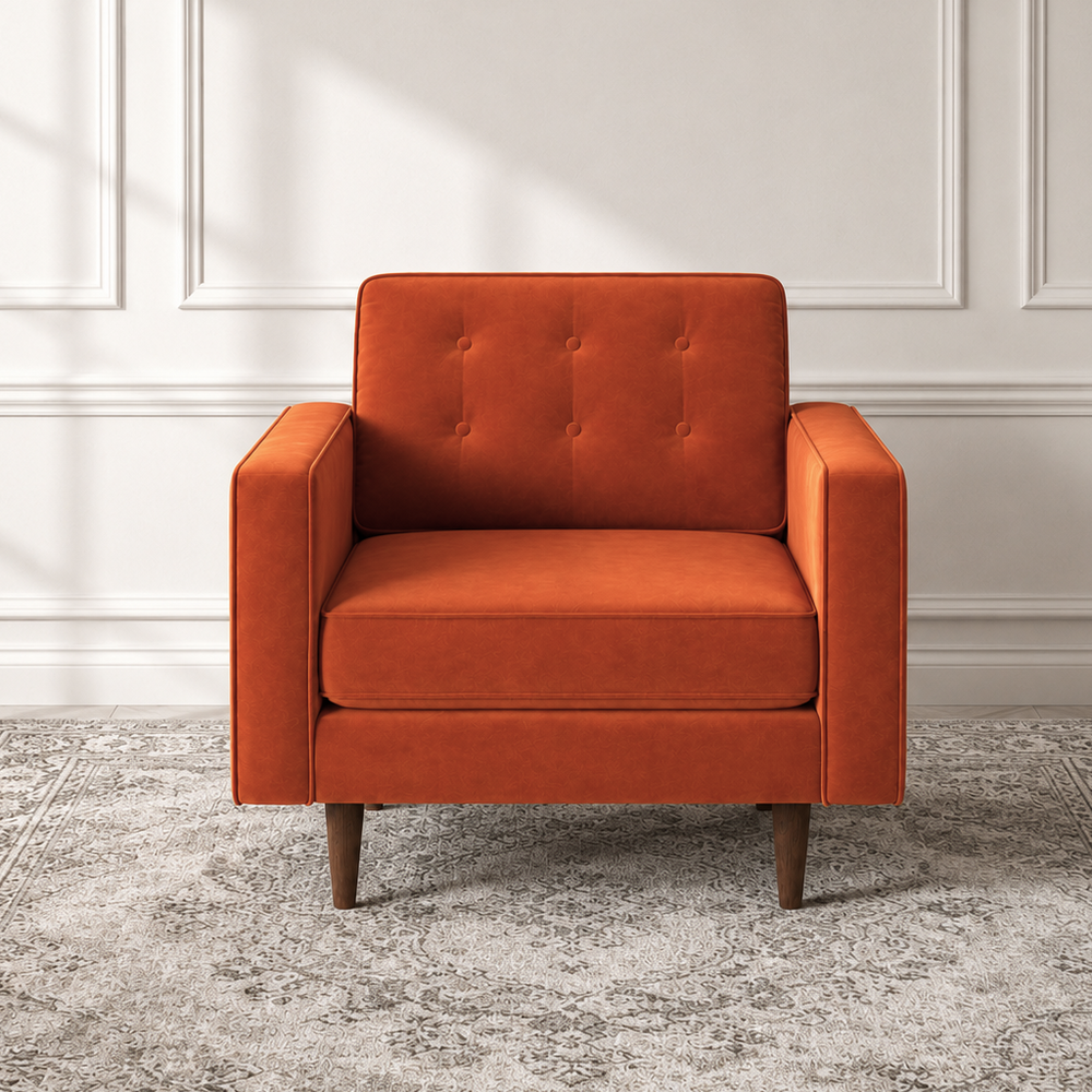 An orange upholstered armchair with a tufted backrest and tapered wooden legs, positioned on a gray patterned area rug against a white paneled wall.