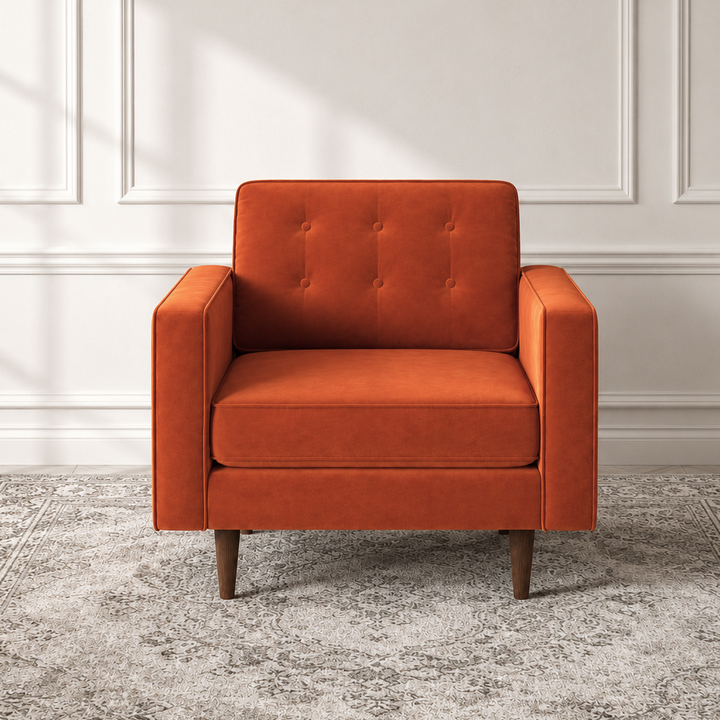 An orange upholstered armchair with a tufted backrest and tapered wooden legs, positioned on a gray patterned area rug against a white paneled wall.