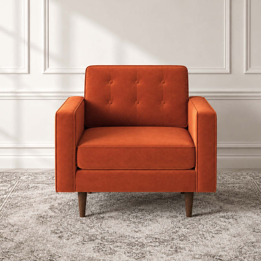 An orange upholstered armchair with a tufted backrest and tapered wooden legs, positioned on a gray patterned area rug against a white paneled wall.